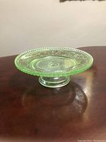 Side angled view of green Depression glass pedestal cake plate showing detailed pattern and clear pedestal base.