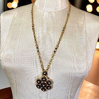 Full view of the necklace displayed on a mannequin, showing gold-tone chain and floral pendant with blue enamel and rhinestones