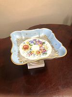 Pedestal candy dish on wooden table showing top section with floral pattern and blue gold border