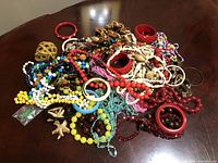 Overview of a large mixed lot of vintage costume jewelry items including multiple necklaces, bracelets, bangles, and earrings in various colors and styles on a wooden table.