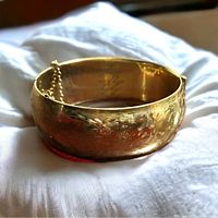 Photo showing the front view of the gold filled bangle with etched floral patterns and attached safety chain.