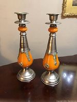 Front view of both orange glass and silver-tone metal Moroccan candle holders on a wooden table.