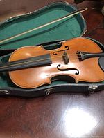 Old violin and bow lying inside a green-lined case, showing the full violin body and bow.