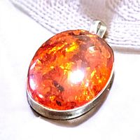 Close-up showing bright orange polished amber cabochon with natural inclusions in a silver bezel set pendant.