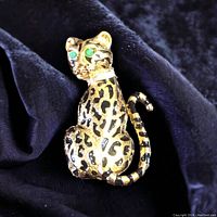 Front of gold-tone vintage cat brooch with black spots and green eyes sitting on black fabric.