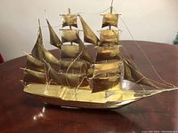 Detailed side views showing the solid brass sailboat with three masts, multiple sails, and rigging on a wooden table.