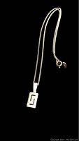 Full image of silver necklace with geometric cut-out rectangular pendant on black background