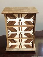 Front view showing the 3 drawers with white and dark wood inlay geometric design and brass knobs.