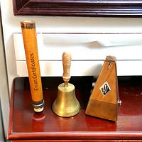 Photo of the vintage wooden exam certificates holder tube, brass hand bell, and wooden mechanical metronome arranged side by side on a wooden surface.