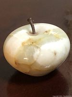 Carved apple-shaped paperweight made of onyx stone, showing natural color veining and dark brown stem on a dark surface.