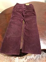 Full length view of burgundy corduroy jeans laid flat on a wooden surface, showing front and general condition.