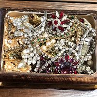 Top-down view inside vintage porcelain jewelry box showing a mix of rhinestone and pearl jewelry including brooches, necklaces, bracelets, and earrings in a compact arrangement.