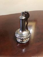 Front and angled view of the vintage Ronson table lighter showing the decorative embossed scrollwork on the metal base and the lever ignition mechanism on top.