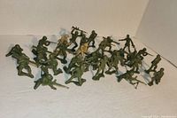 Wide shot showing about 27 plastic army men figurines in various standing, kneeling, and prone poses with weapons.