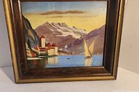 Framed painting on wood panel showing a lakeside castle and sailboat with snowy mountains in the background