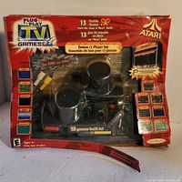 Full front view of Atari Plug & Play package with paddle controllers visible and 13 games listed on box. Packaging is damaged.