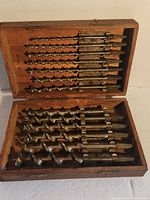 Top view of wooden box open showing upper layer of auger bits arranged by size