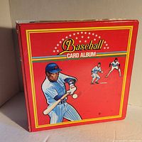 Front and spine of a red baseball card album binder showing baseball players illustrations and title Baseball Card Album.