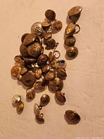 Overview of many vintage metal buttons on white surface showing variety of sizes and designs.