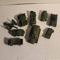 Various worn green military Dinky Toys vehicles and toy cannon laid out on white surface, showing condition and paint wear