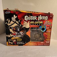 Front view of boxed Guitar Hero Air Guitar Rocker toy by Jada Toys showing graphics and toy visible through clear window.