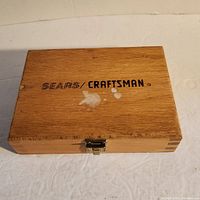 Closed wooden box with Sears Craftsman label on the lid, showing wear and paint marks.