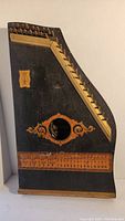 Full view of the mandolin harp showing the trapezoidal black wooden body, strings on top right, decorative painted sound hole, and printed musical scale near the bottom.