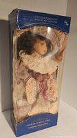 Front view of the porcelain doll in original packaging with visible facial features and outfit details.