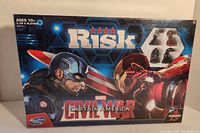 Front of the box showing Risk logo, Captain America and Iron Man artwork, and visible game pieces inside packaging.