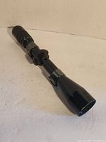 Side angled view of black Bushnell Sportview rifle scope on white surface.