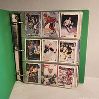 Open green binder displaying sports cards inside plastic sleeve with nine cards visible.