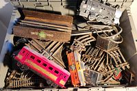 Overview of the train set showing multiple tracks, red and orange carriages, black locomotive, brown flatbed, and small grey container inside a plastic crate.