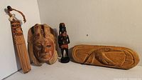 Overview of the four wood carving art pieces including comb, mask, figurine, and relief panel against a plain background.