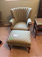 Front view showing the armchair's scalloped, vertically channeled back and rolled arms with wooden trim, paired with the matching footstool in patterned fabric and wooden legs.