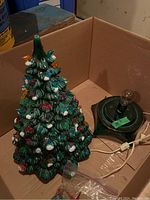 Vintage ceramic Christmas tree with green base, light bulb attached, and various spare bulbs in a bag beside it, all inside a box.
