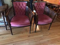 Two matching wood chairs with cane sides and back, upholstered in dusty rose fabric with tufted back cushions, placed on hardwood floor.