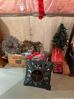 Photo showing entire lot with tree stand, wreaths, artificial tree, and boxes of ornaments and decorations in a basement setting