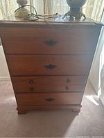 Front view of wood dresser with four drawers and metal pulls, items on top include lamps not included in sale.