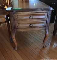 Front and angled view of wooden end table showing two drawers with metal ring pulls and curved legs, water stain visible on top corner.