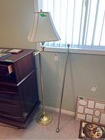 Floor lamp beside wooden dresser, showing fabric lamp shade and metal round weighted base, with an extra metal pole on the side.