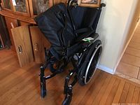 Full view of black folding wheelchair showing seat, backrest, armrests, and wheels.