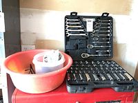 Full socket set and wrenches in open black plastic case with red basin beside on tool chest