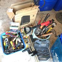 Photo showing plastic bin and cardboard box filled with hand tools, hammers, ratchets, and Skilsaw cutter.