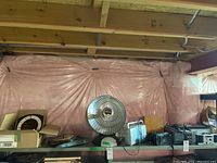 Shelf display of multiple electronics and timepieces including heating fan, radios, TV, and clocks on a metal shelf against pink plastic sheeting in a basement.