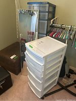 Photo showing full-length wall mirror with metal frame, white plastic storage drawers on casters, and part of laminate shoe storage unit.