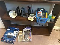 Full lot view showing items on bookshelf and labeled boxes for label makers and calculator on floor