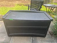 Front view of a dark brown resin outdoor storage box with woven pattern design, showing the lid and front surface.