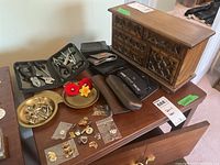 Photo of wooden jewelry box with brass change trays, vintage pins, manicure tool kits, and small wallets on a wooden surface.