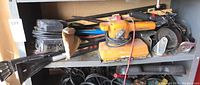 Overview photo showing a shelf containing 2 orange dual motor Black & Decker sanders, Black and red cordless screwdriver, metal tools including a crowbar, and other miscellaneous items.
