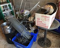 Wide shot showing birdbath, metal screening rolls, blue recycling bins filled with various scrap metal, and a box containing bakeware tins and other metal items.